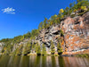 A view of the steep rocky cliffs of Barron Canyon in Algonquin Provincial Park, reflected in the calm waters of the Barron River under a clear blue sky — captured during a kayaking trip with NERIS Folding Kayaks